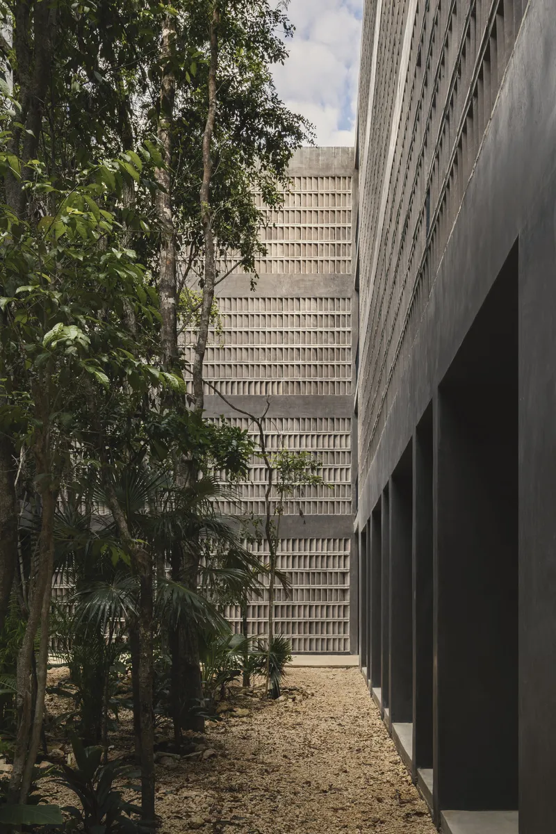 Concrete breeze block facade tower framed by jungle vegetation and smooth grey walls