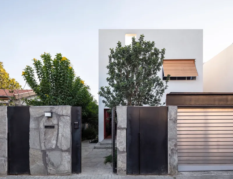 Street facade with stone-clad entry wall and black steel gate framing the white volume beyond