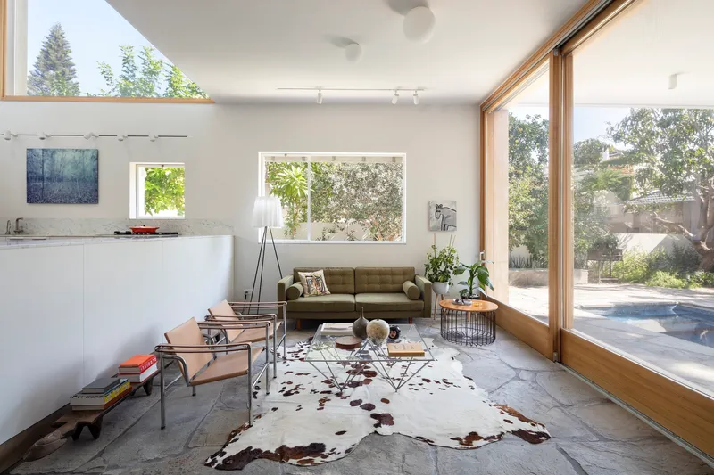 Living room with floor-to-ceiling timber-framed glazing opening to poolside courtyard with established tree
