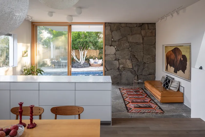 Interior view showing rough stone accent wall beside timber-framed door opening to pool with white-barked tree