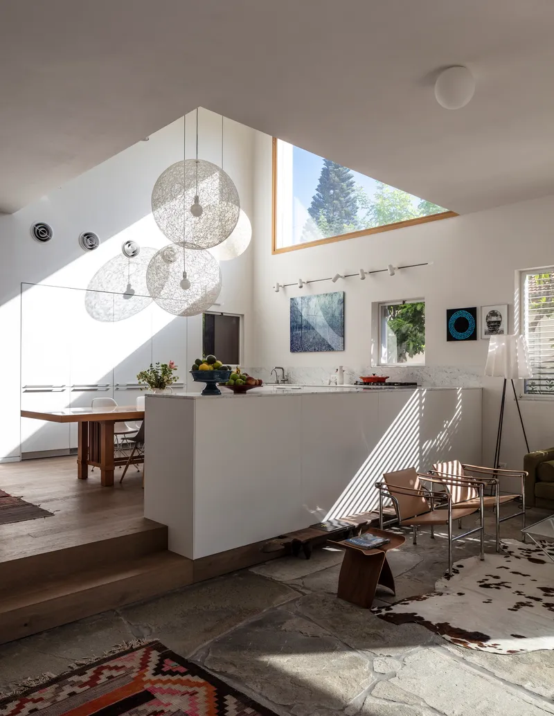 Open kitchen and living area with white island and triangular skylight casting afternoon shadows