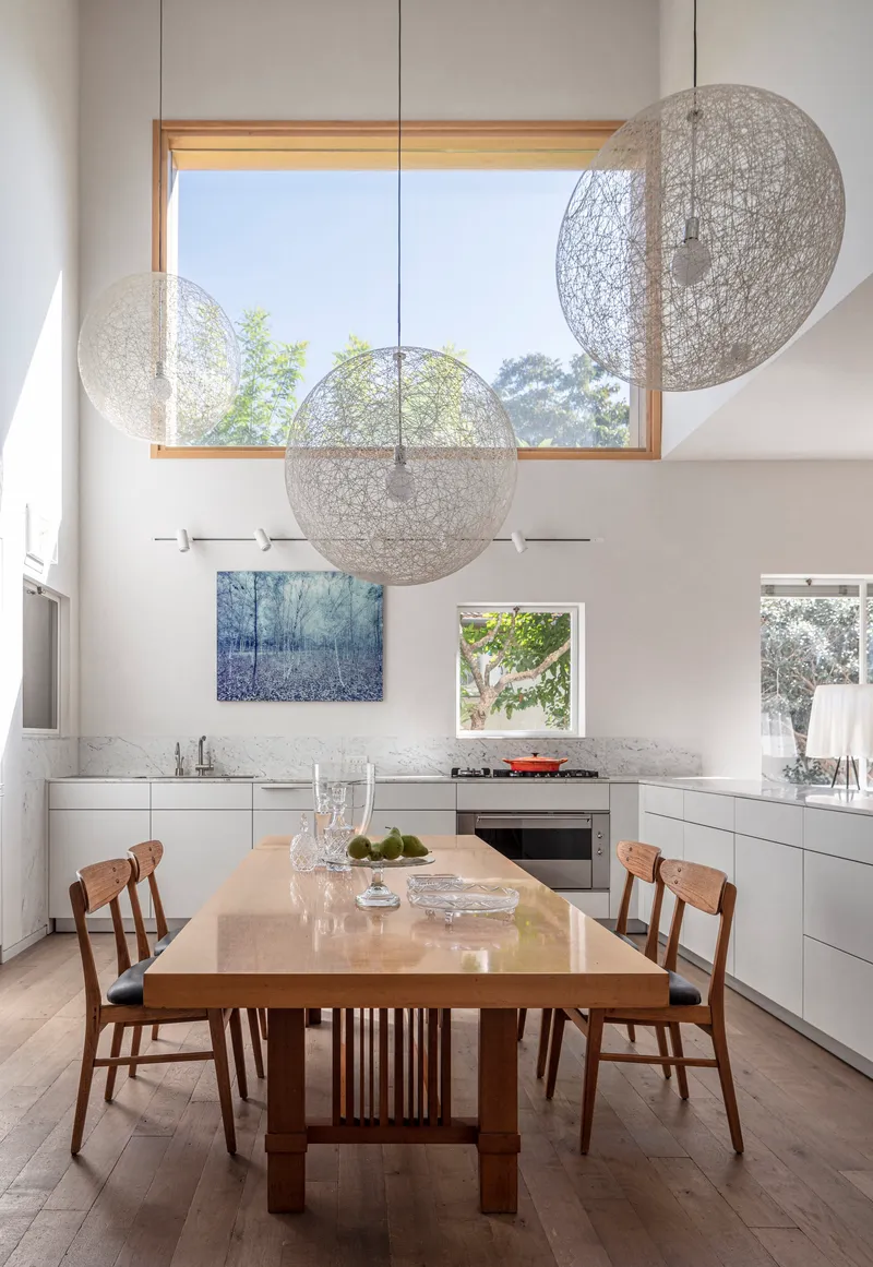 Dining table beneath three spherical pendant lights and timber-framed clerestory window