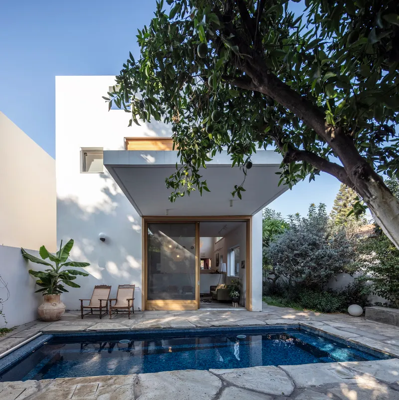 Rear facade with timber-framed glazing opening to the pool courtyard under dappled tree shade