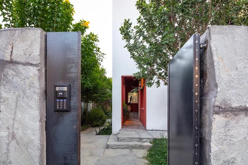 Entry gate with steel panels set between rough stone piers and view to red threshold