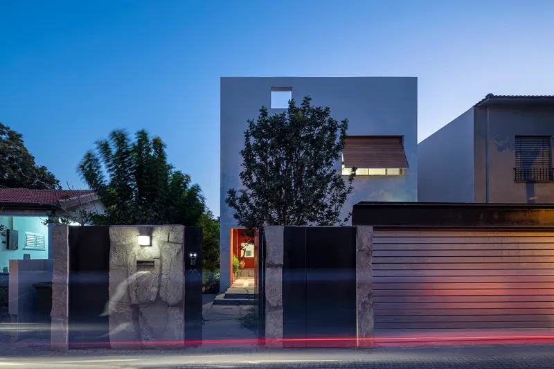 Street facade with black metal gate and gray volumes behind at twilight with light trails