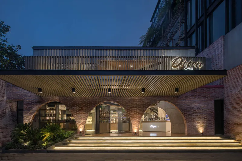 Street facade at dusk showing arched brick openings beneath illuminated timber slat canopy and neon signage