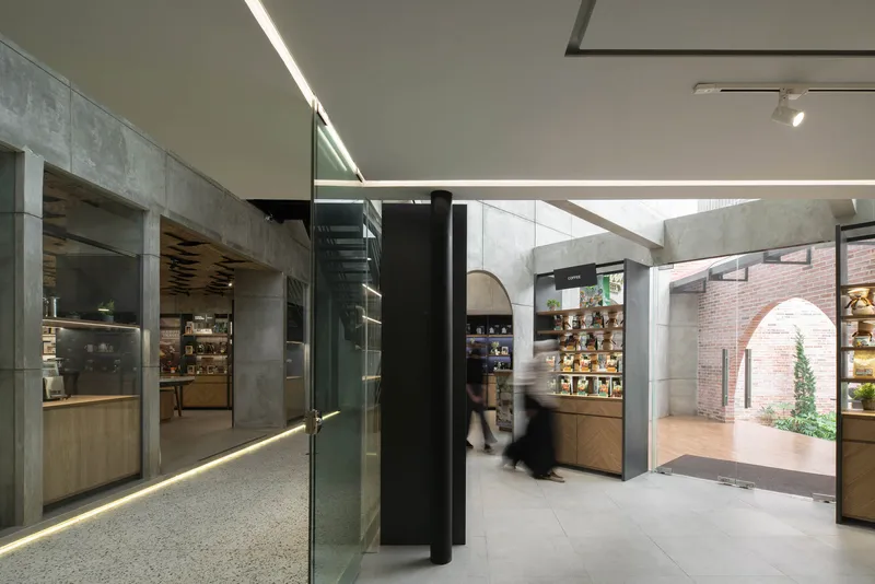 Retail interior with concrete walls, glass partitions, and a blurred figure walking through the terrazzo-floored corridor