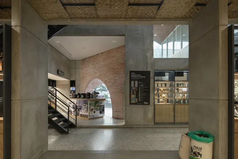 Double-height space with metal staircase leading to mezzanine beneath a woven ceiling panel