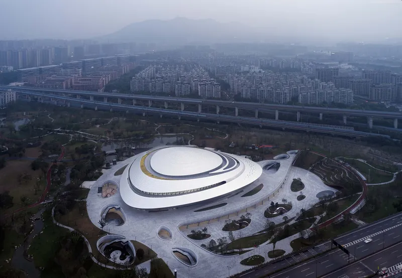 Aerial view of the oval white roof with concentric bands surrounded by landscaped grounds and distant mountains