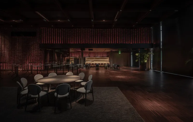 Event hall with woven screen wall and scattered round tables under a coffered timber ceiling at night