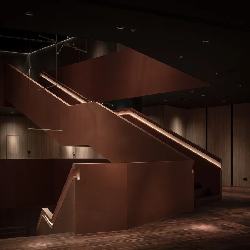 Folded copper-clad staircase with integrated handrail lighting in a dark double-height interior