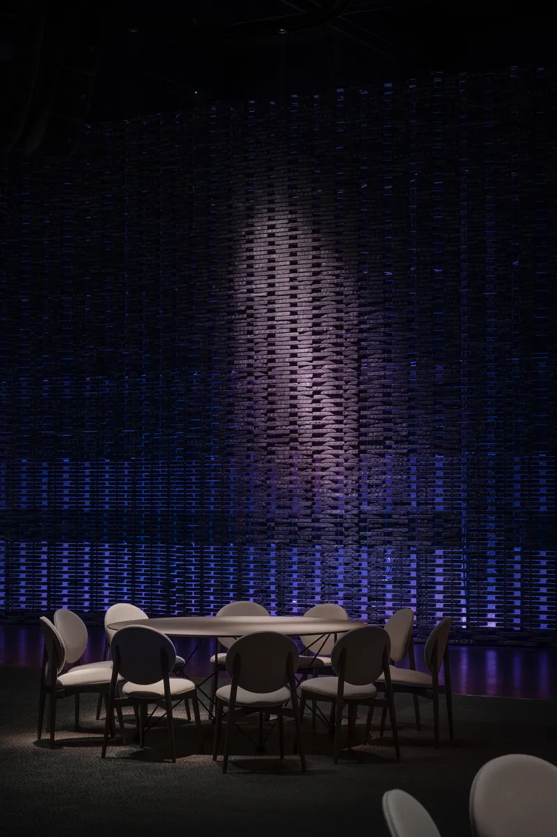 Textured wall installation with vertical relief pattern lit in blue and violet behind a dining table