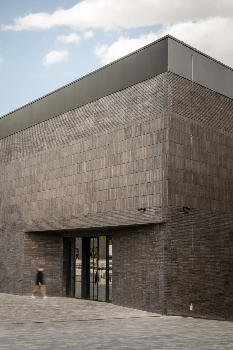 Corner entrance with two-tone brick cladding and recessed glass doors as a figure passes