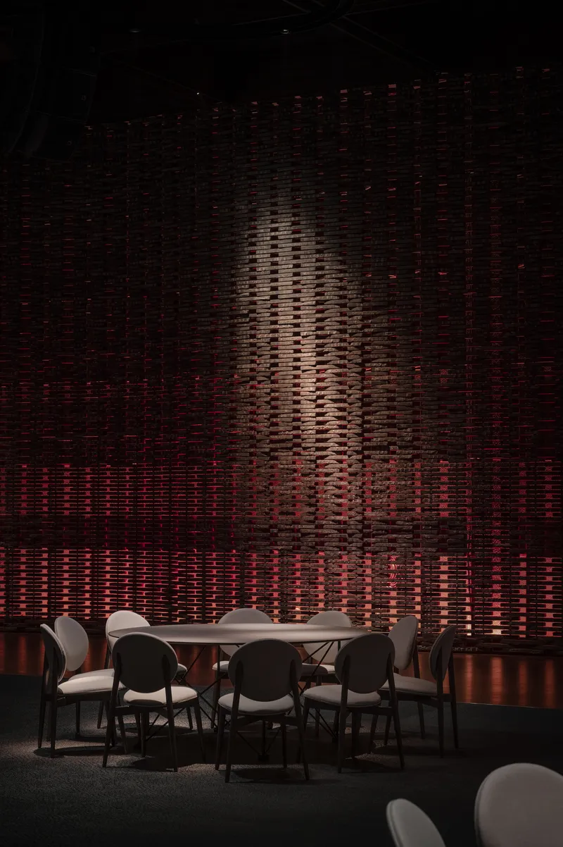 Textured wall installation with vertical relief pattern lit in amber and red behind a dining table