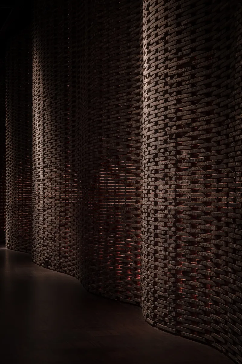 Curving brick wall with basket-weave pattern illuminated by dramatic sidelight in a dark interior corridor