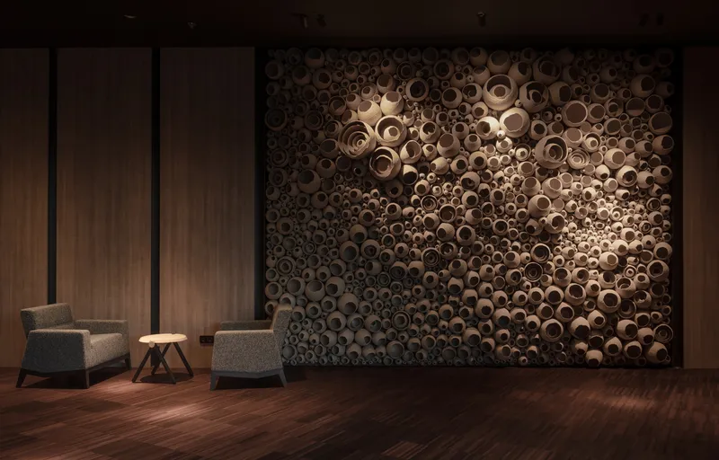 Sculptural wall installation of clustered cylindrical timber tubes backlit against wood paneling with two lounge chairs