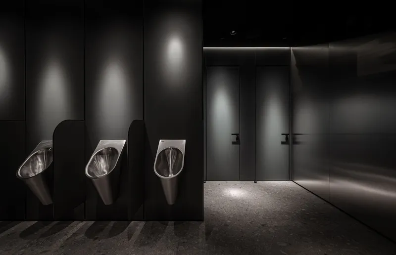 Dark restroom interior with three stainless steel urinals and backlit wall panels