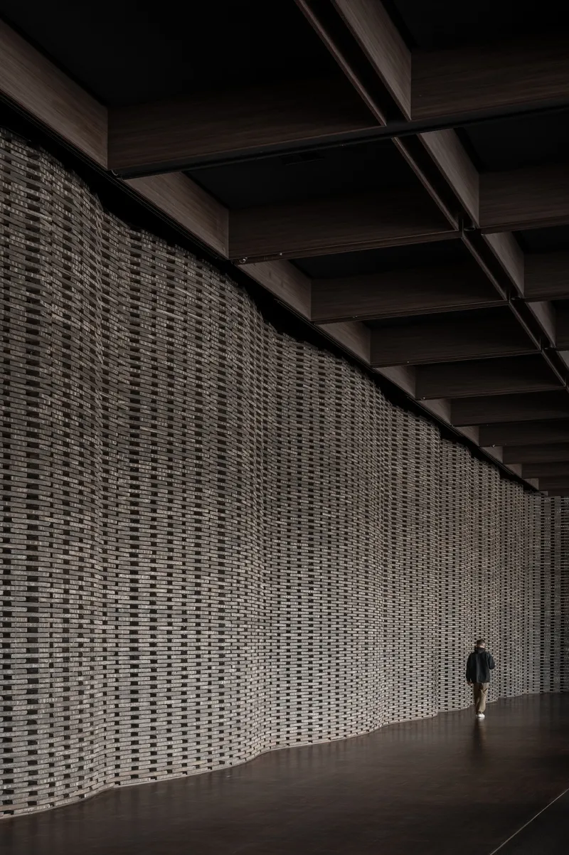 Long perforated brick screen wall with coffered timber ceiling and a lone figure walking