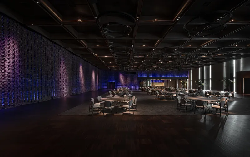Event hall with woven wall panels illuminated in purple and blue and scattered dining tables