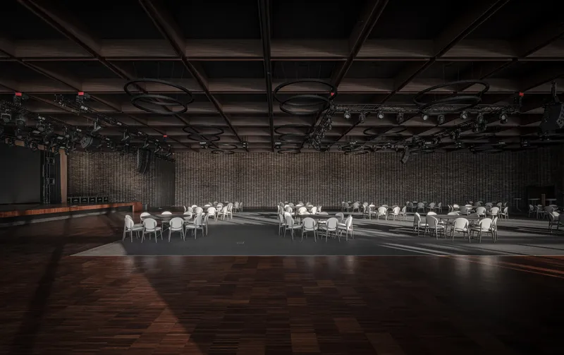 Large banquet hall with exposed ceiling rigging and round tables on dark timber flooring