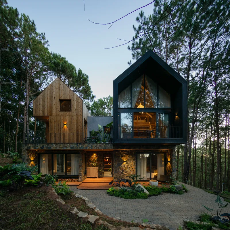 Front facade showing timber and dark metal gabled volumes above a stone base at dusk