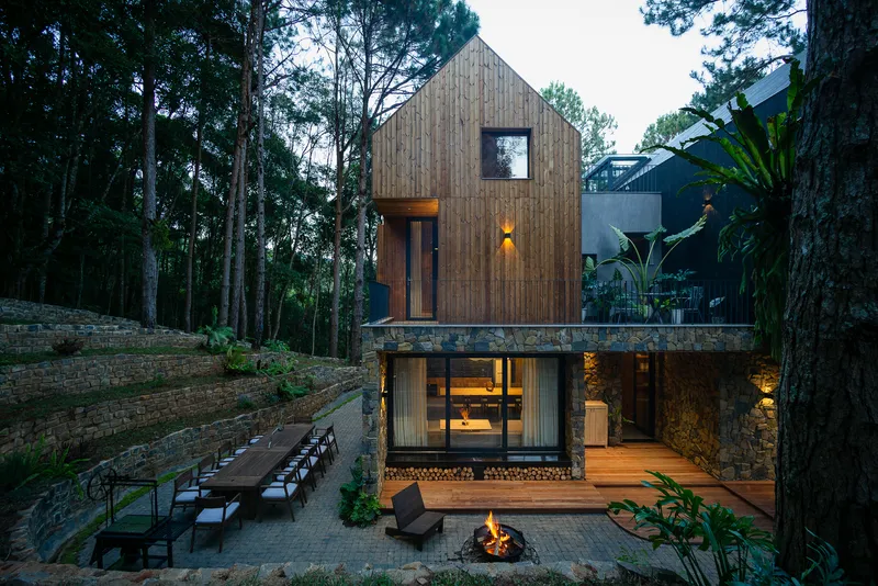 Rear courtyard at dusk with fire pit and terraced stone amphitheater steps below timber gable volumes