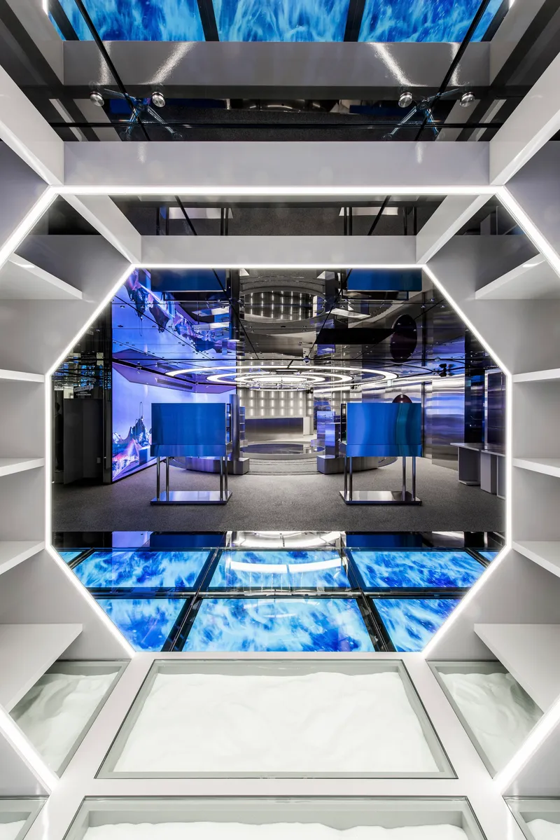 Looking down through octagonal void with glass floor panels and blue digital screens