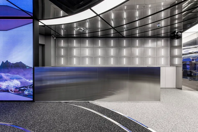 Brushed steel reception desk beneath a quilted metal panel ceiling with recessed linear lighting