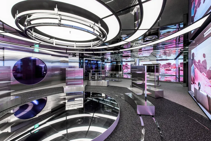Display area with curved glass partitions and circular ceiling element beneath reflective black soffit