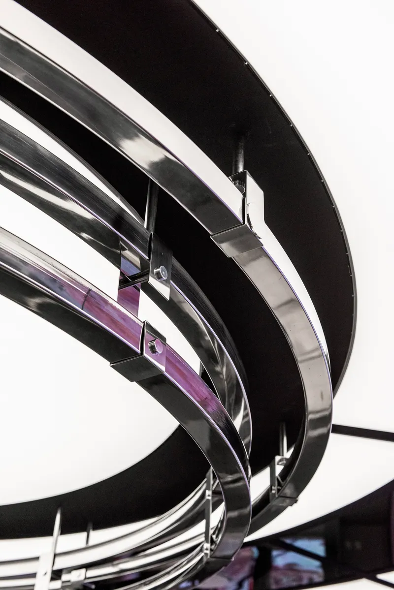 Close-up of curved black metal banding wrapping around purple glass panels in an interior stairwell