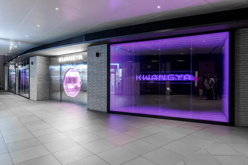 Retail storefront with purple LED-lit glass facade and grey brick walls along a mall corridor