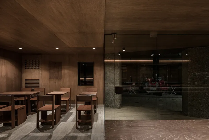 Seating area with wooden tables and glass partition separating dining from service counter