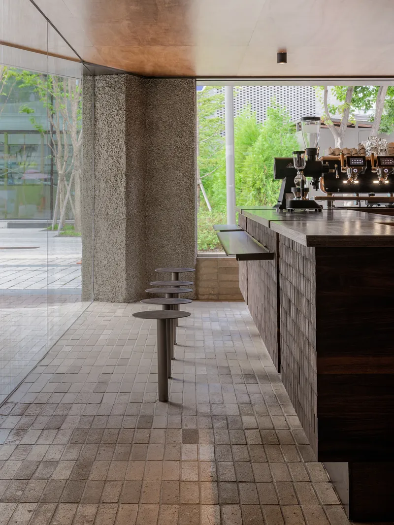 Rough stone wall beside a counter with circular metal stools overlooking a planted courtyard through large windows