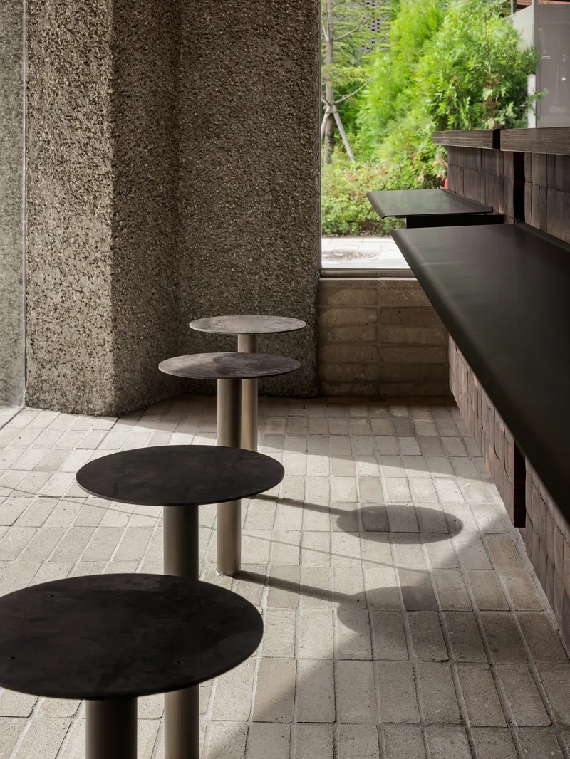 Close-up of four circular stools with metal stems aligned along a counter beneath textured stone walls