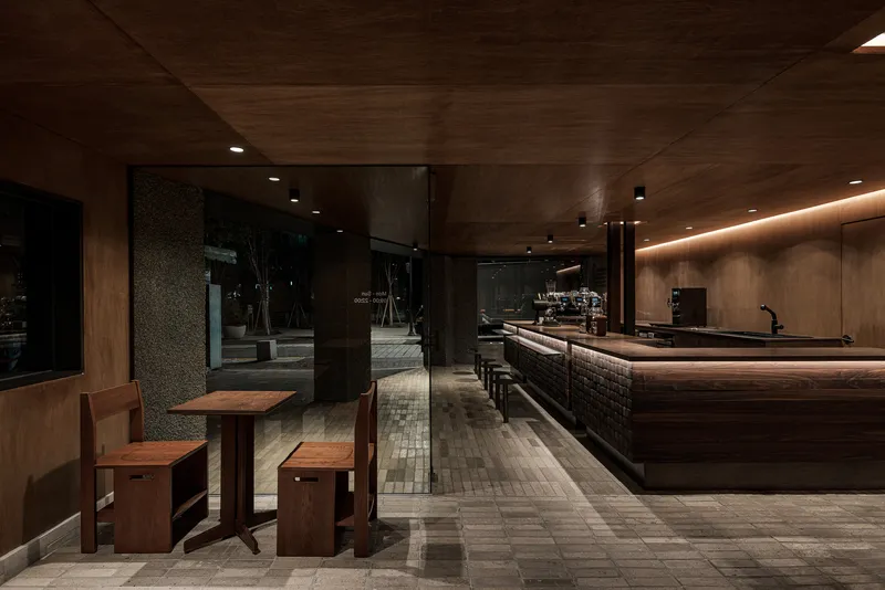 View through the entrance towards the long counter bar with dark tile base and wood seating