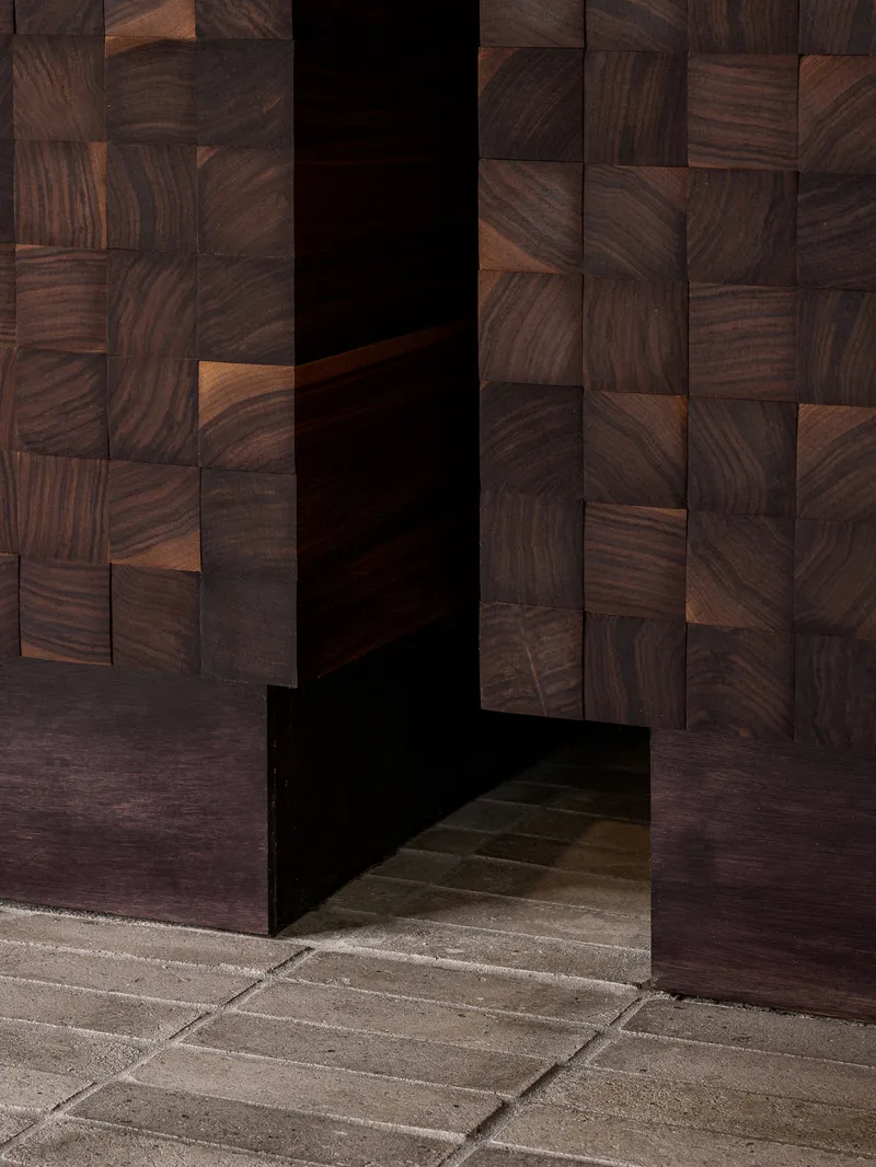 Threshold between stone pavers and dark walnut mosaic wall panels framing a recessed doorway