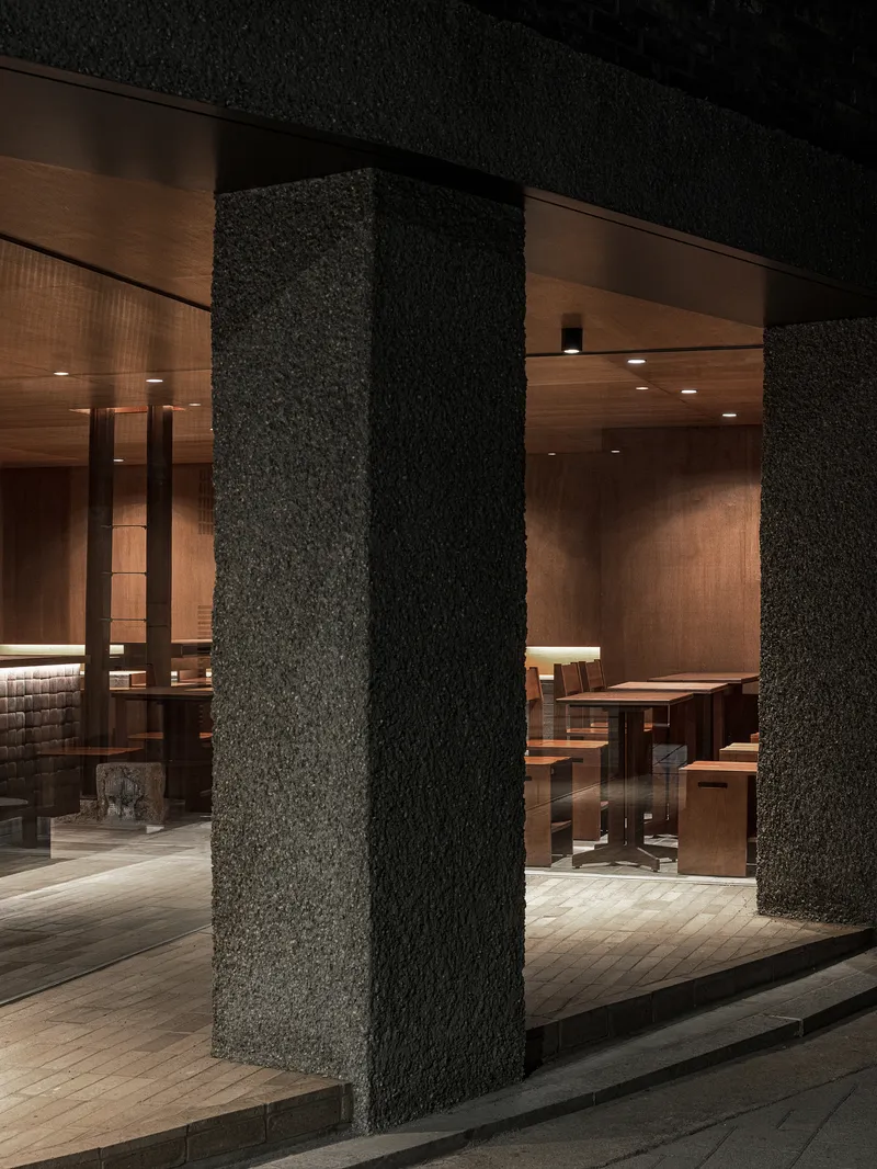 Textured black stone columns supporting the ceiling at the entrance to the dining space at night