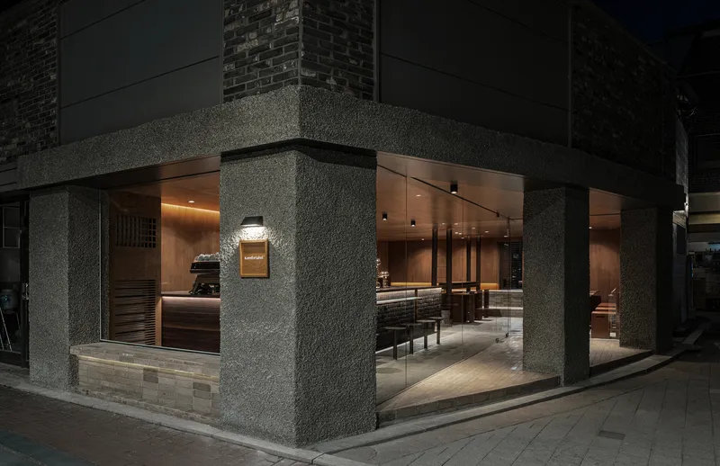 Corner storefront with rough stone columns and floor-to-ceiling glass revealing the interior at night