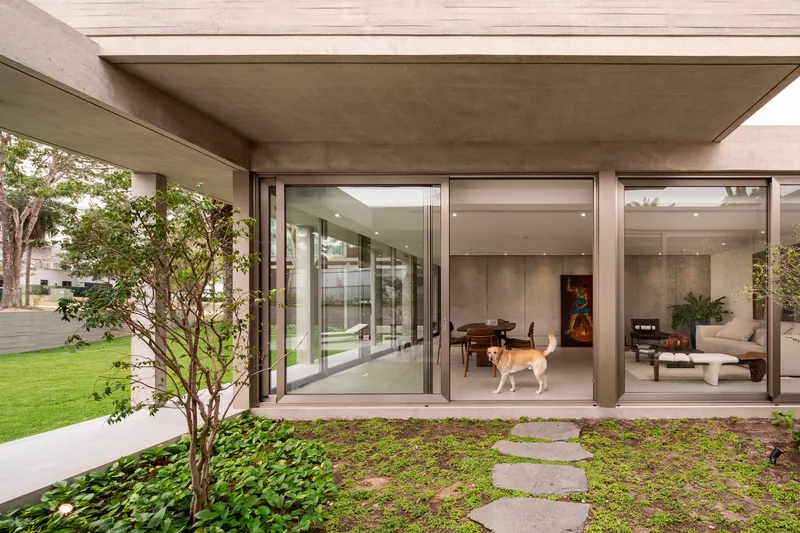 Covered outdoor space with concrete soffit, floor-to-ceiling glazing, dog inside, and planted courtyard garden