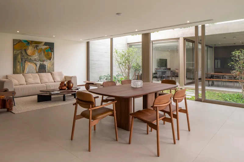 Open-plan dining and living area with timber table, terrazzo flooring, and views to planted courtyards