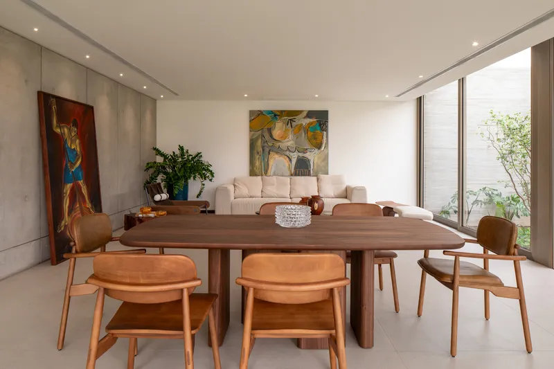 Open-plan dining and living area with timber table and concrete wall alongside a planted courtyard