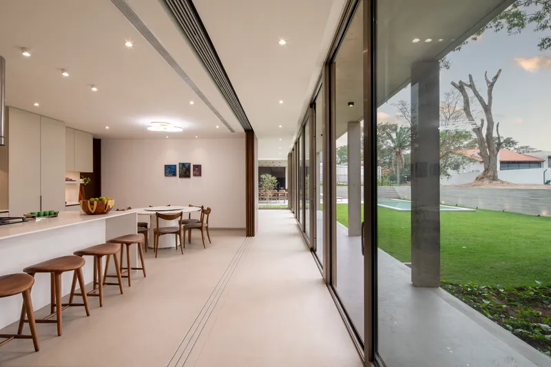 Kitchen and dining space with floor-to-ceiling glazing opening onto a lawn and pool