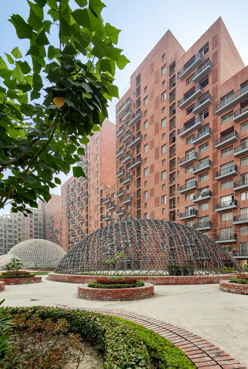 Steel geodesic dome in a courtyard plaza with residential towers and green foliage in the foreground