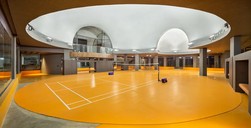Indoor sports court with bright orange flooring beneath a circular white ceiling with skylights