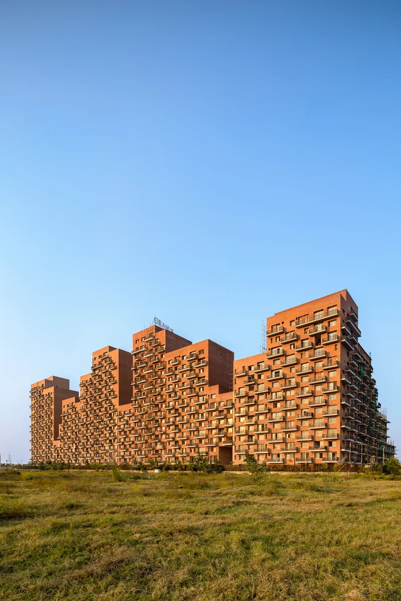 Stepped brick residential blocks rising from an open grass field in afternoon light