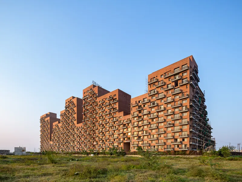 Stepped brick residential towers with recessed balconies rising from an open grassland under clear sky