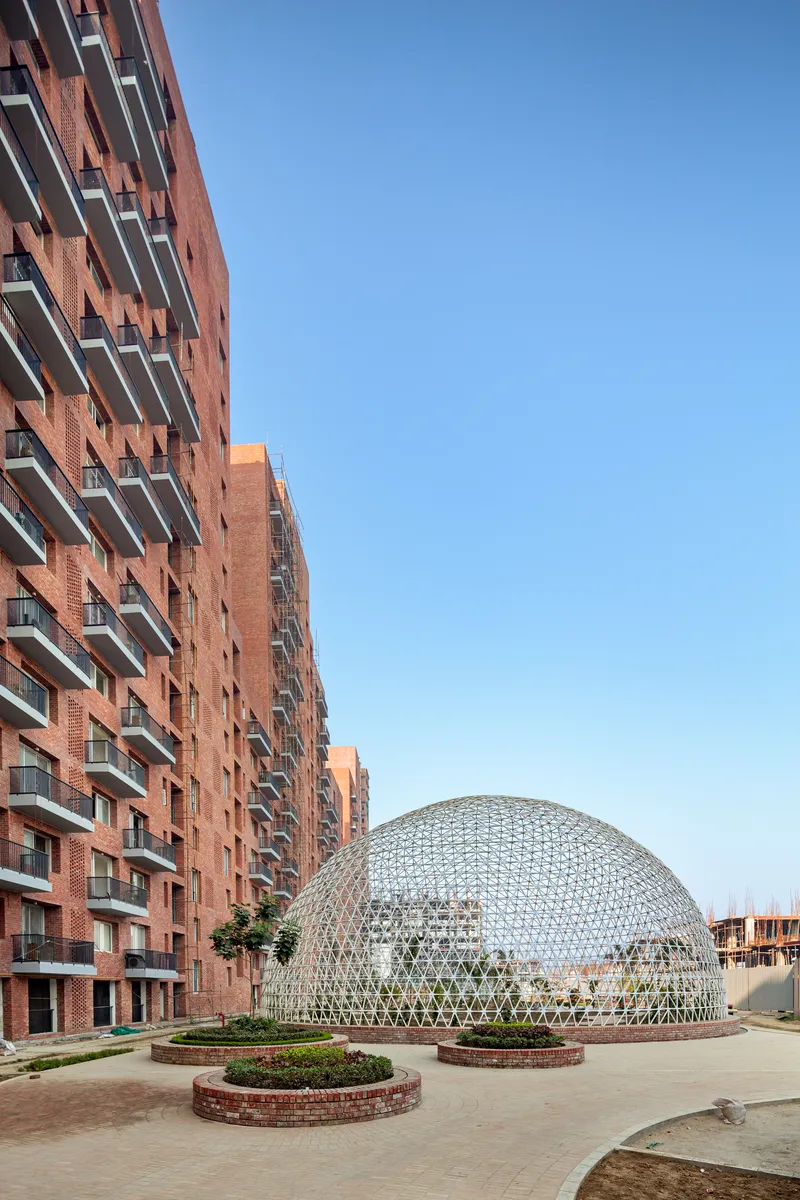 White geodesic dome beside brick towers with circular planted beds in the foreground under clear sky