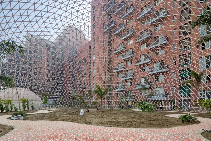 Interior view through triangulated steel lattice structure enclosing planted beds with palms and residential towers beyond