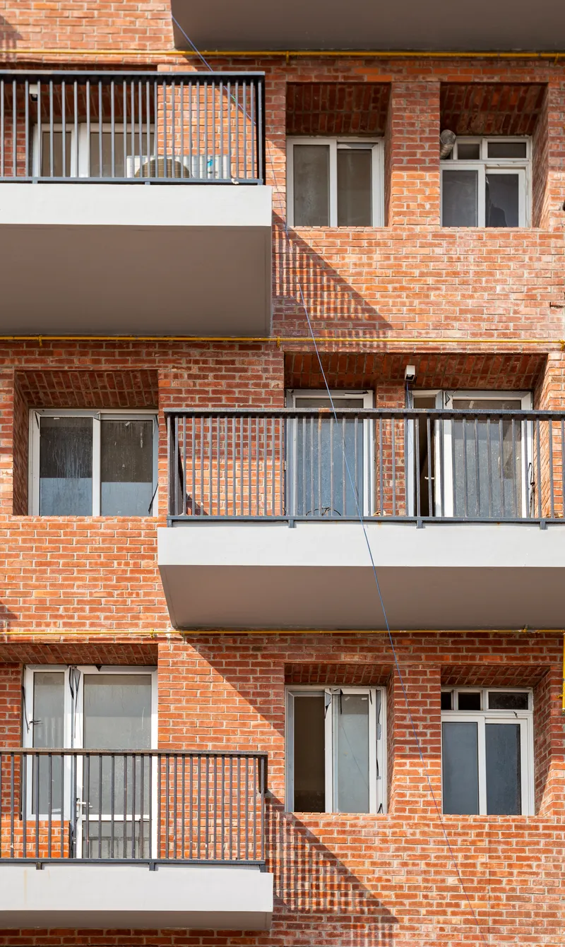 Facade detail showing stacked balconies with metal railings and brick panels forming diagonal shadow lines