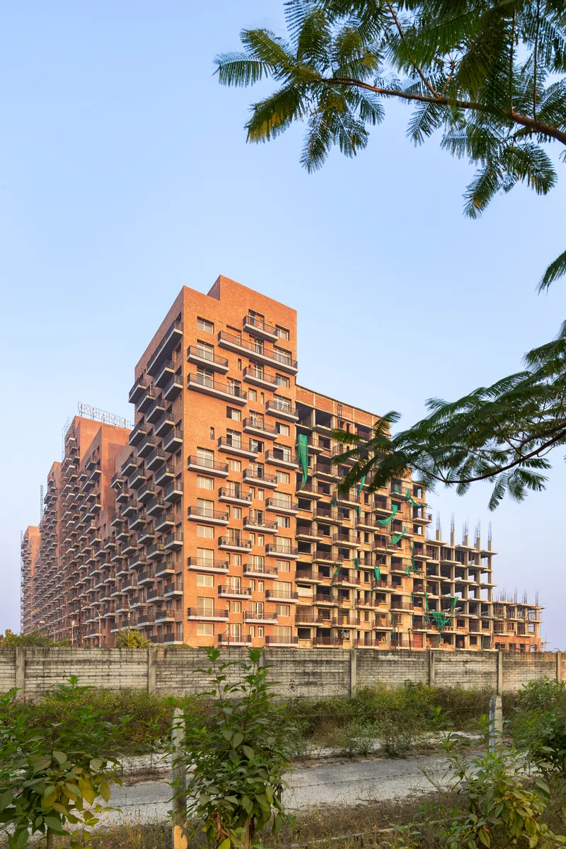 Corner view of the cascading brick towers with deep balconies, framed by palm trees in the foreground